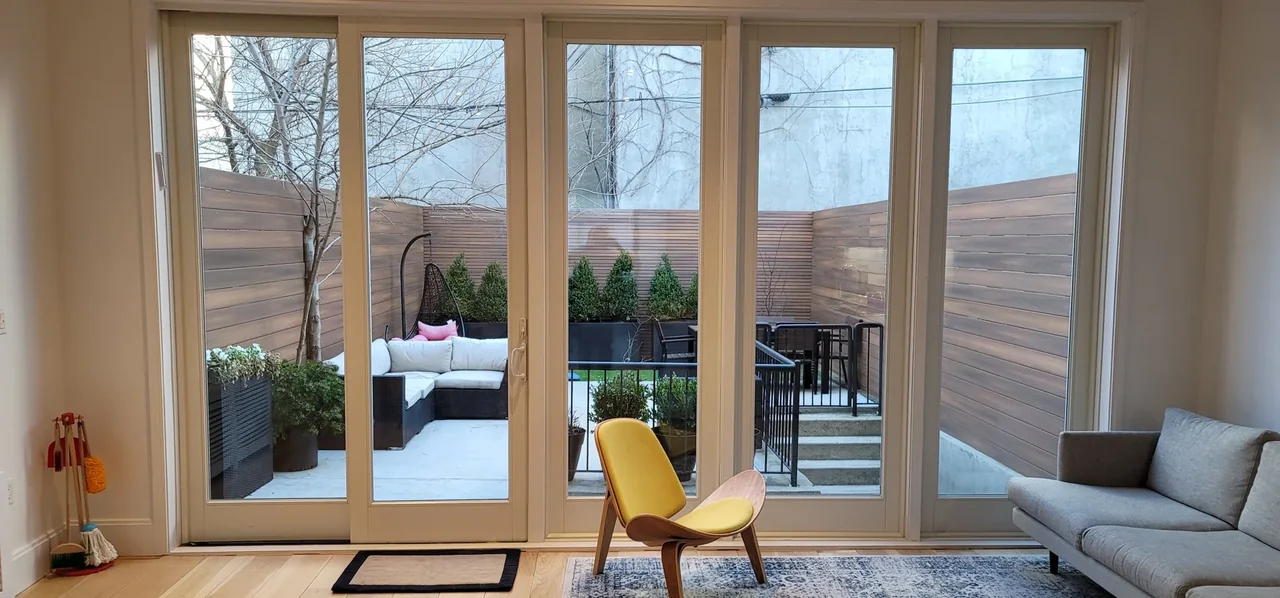 Skillman Street Brooklyn garden patio with horizontal privacy fencing and outdoor lounge seating, viewed through glass doors